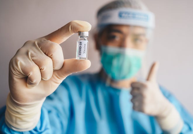 Healthcare professional holding a COVID-19 vaccine vial while giving a thumb up