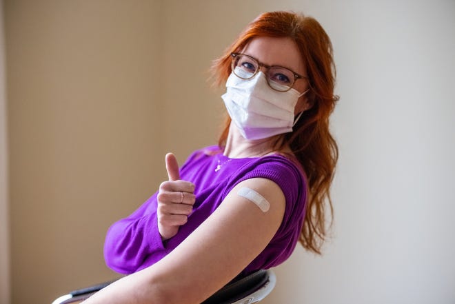 Woman wearing face mask looking at camera showing thumbs up after getting the covid-19 vaccine. Female gesturing thumbs-up sign after getting coronavirus vaccine at vaccination center.